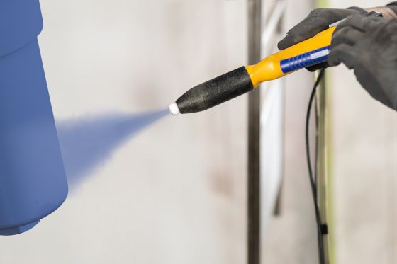 A spray gun powder coating a part in blue